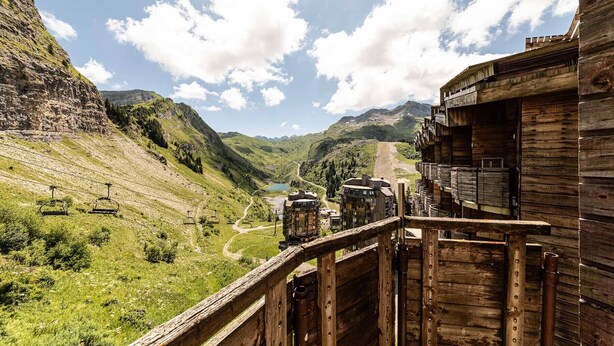 Ein Holzbauten mit Blick auf eine gebirgige Landschaft und einer Seilbahn im Hintergrund.