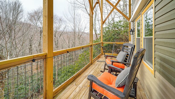 Eine Holzterrasse mit zwei Stühlen und einem Tisch, mit Blick auf eine bewaldete Gegend.