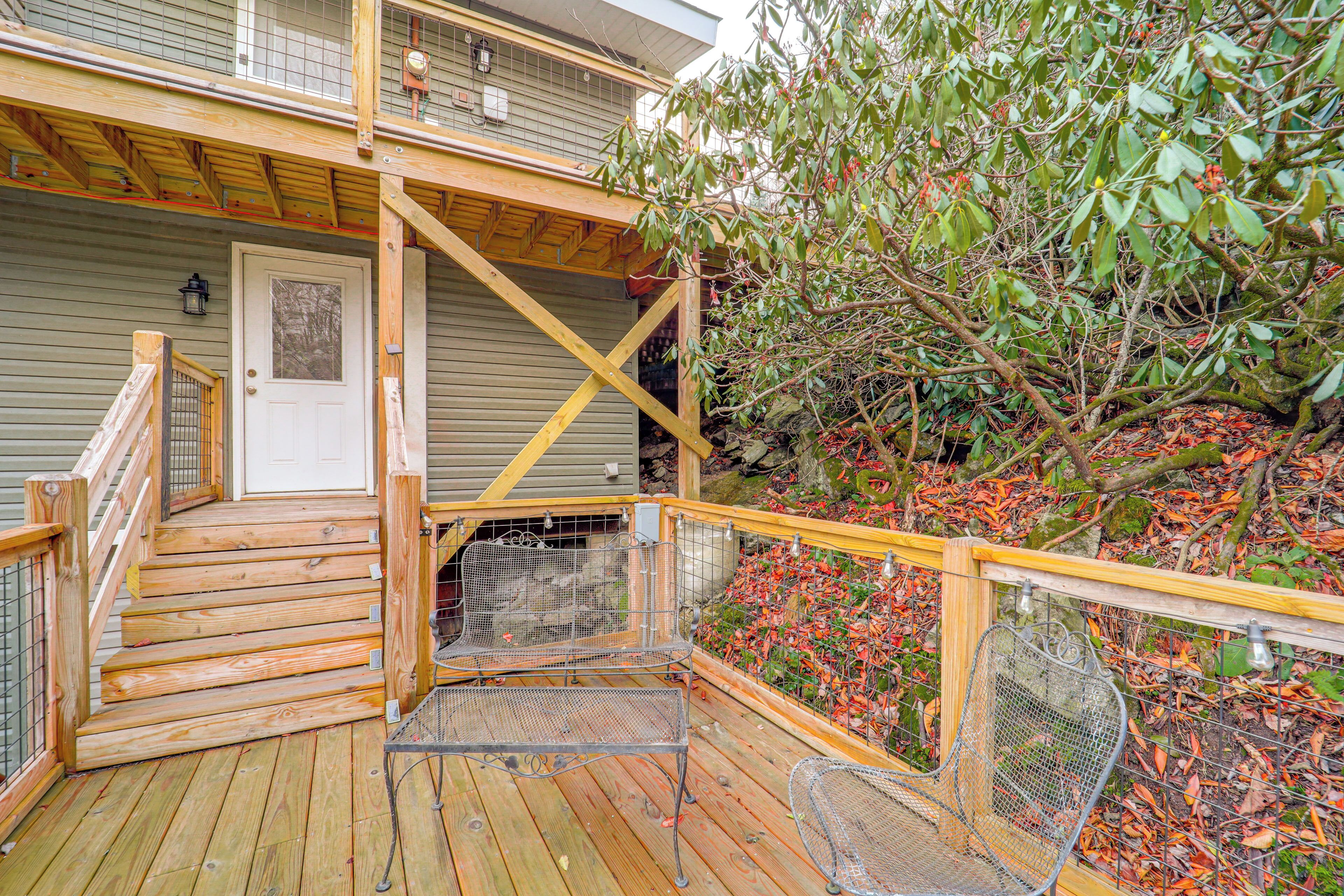 Une terrasse en bois avec une rambarde en métal, une porte et un petit espace aménagé pour s’asseoir à l’extérieur.