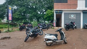 Uma estrada de terra leva a um edifício com uma placa indicando Panakal Park Homestay. Várias motocicletas estão estacionadas em frente ao edifício.