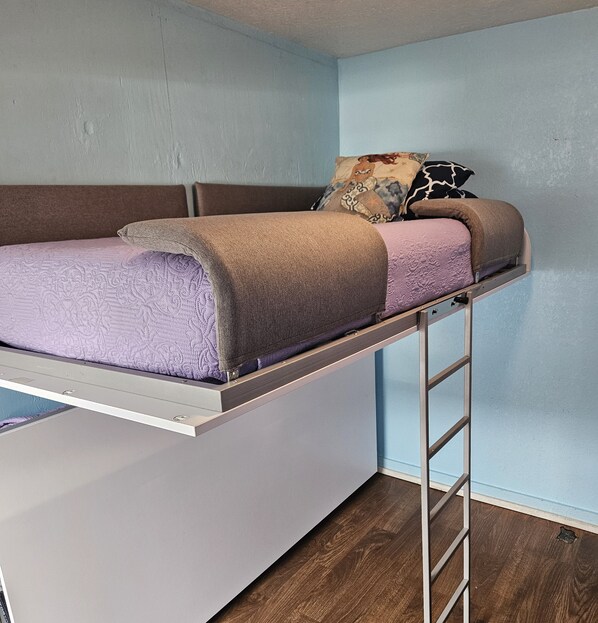 Uma cama beliche com escada, um cobertor roxo e almofadas estampadas.