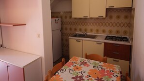 Une cuisine compacte équipée d’un réfrigérateur, d’un évier et d’une cuisinière. On y trouve une table à manger avec des chaises, ainsi qu’un mur recouvert de carreaux décoratifs.