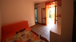 Une chambre à coucher avec un lit, un bureau et une salle de bain visible à travers une porte ouverte.
