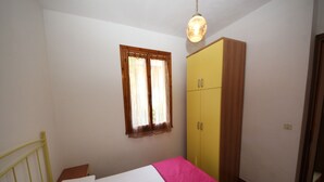 Une chambre à coucher avec un lit, une armoire jaune, une fenêtre avec des rideaux et un luminaire suspendu.