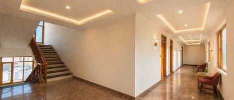 A spacious hallway with a staircase, recessed ceiling lighting, and a view to the outside.