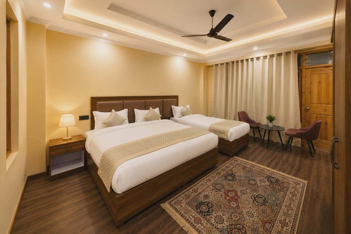 Ein Hotelzimmer mit einem großen Bett, zwei Nachttischen, einem Schreibtisch mit Stühlen, einem Deckenventilator und einem gemusterten Teppich.