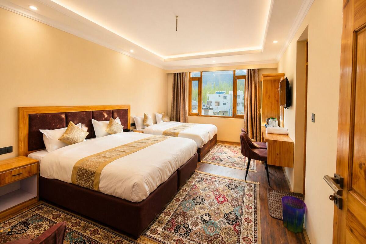Ein Hotelzimmer mit zwei Betten, einem Schreibtisch, einem Sessel, einem Fernseher und einem Fenster mit Blick auf Gebäude.