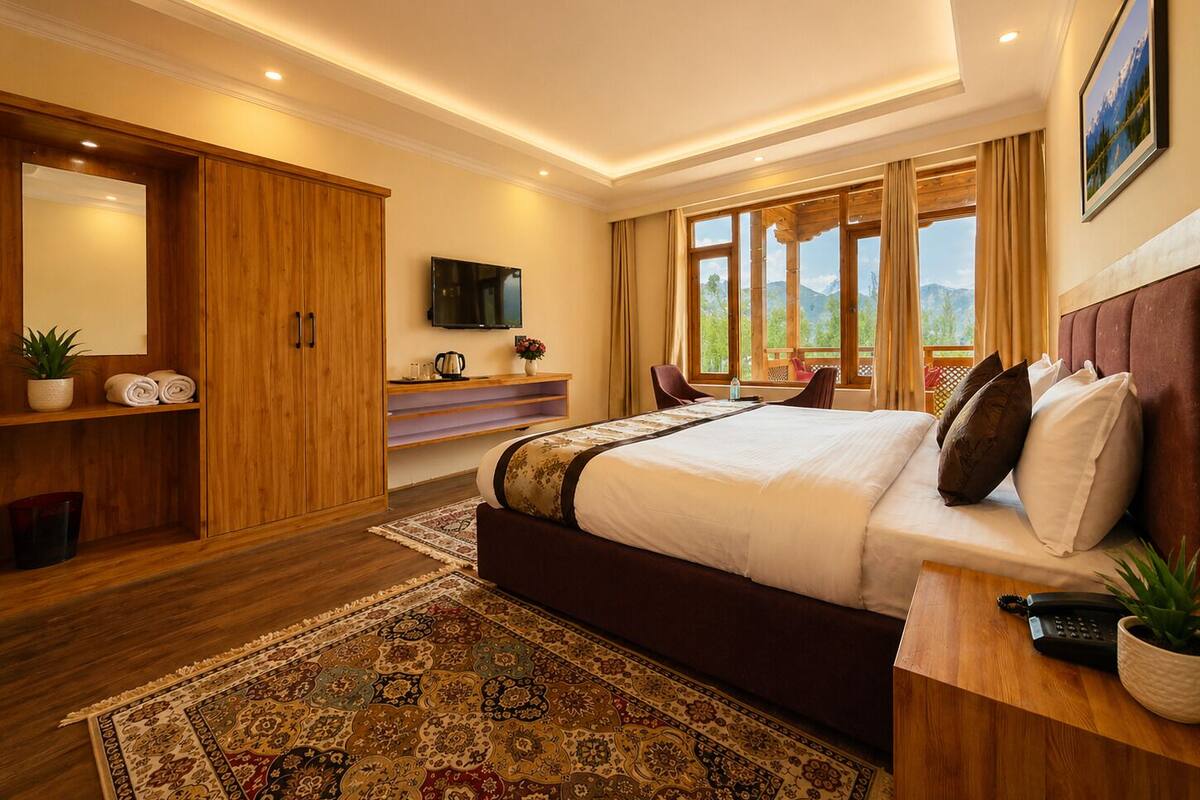 Ein Schlafzimmer mit einem großen Bett, einem Fernseher, einem Holzschrank, einem Schreibtisch mit Stuhl und Blick ins Freie.