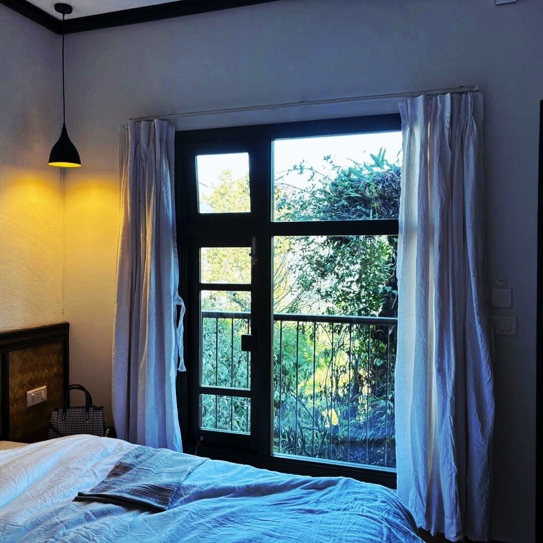 Ein Zimmer mit einem Bett, einer Hängelampe und einem Fenster mit Vorhängen.