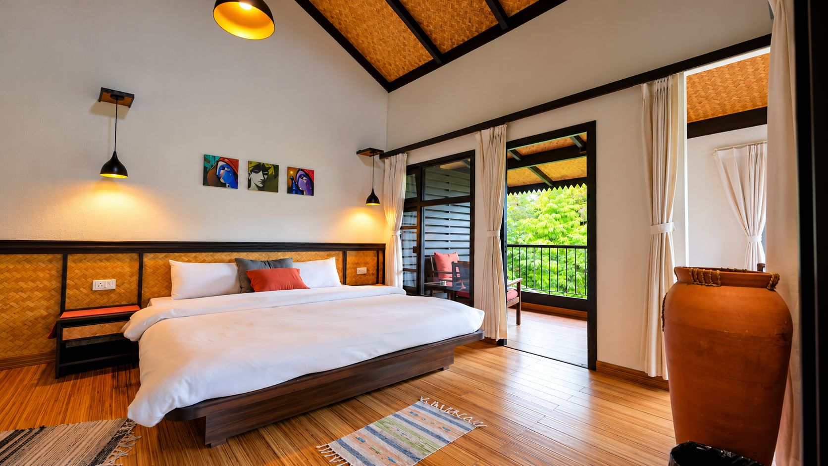 A bedroom with a bed, bedside tables, a nightstand, a window with curtains, and a view of greenery outside.