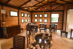A rustic interior with wooden walls, multiple windows, a stone fireplace, and a dining area with tables and chairs. - RedPanda Jungle Camp (Gyalshing)