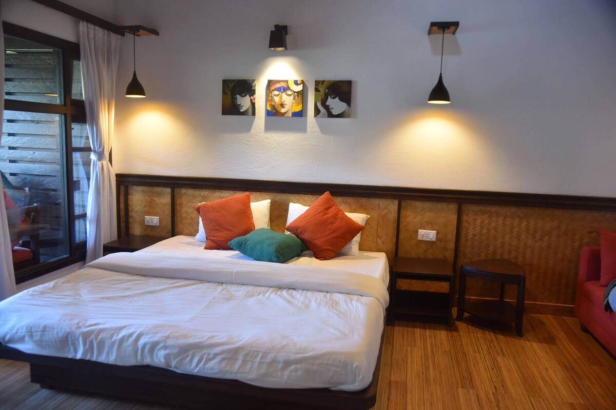 A hotel room with a large bed, two bedside tables, a red chair, and artwork on the wall.