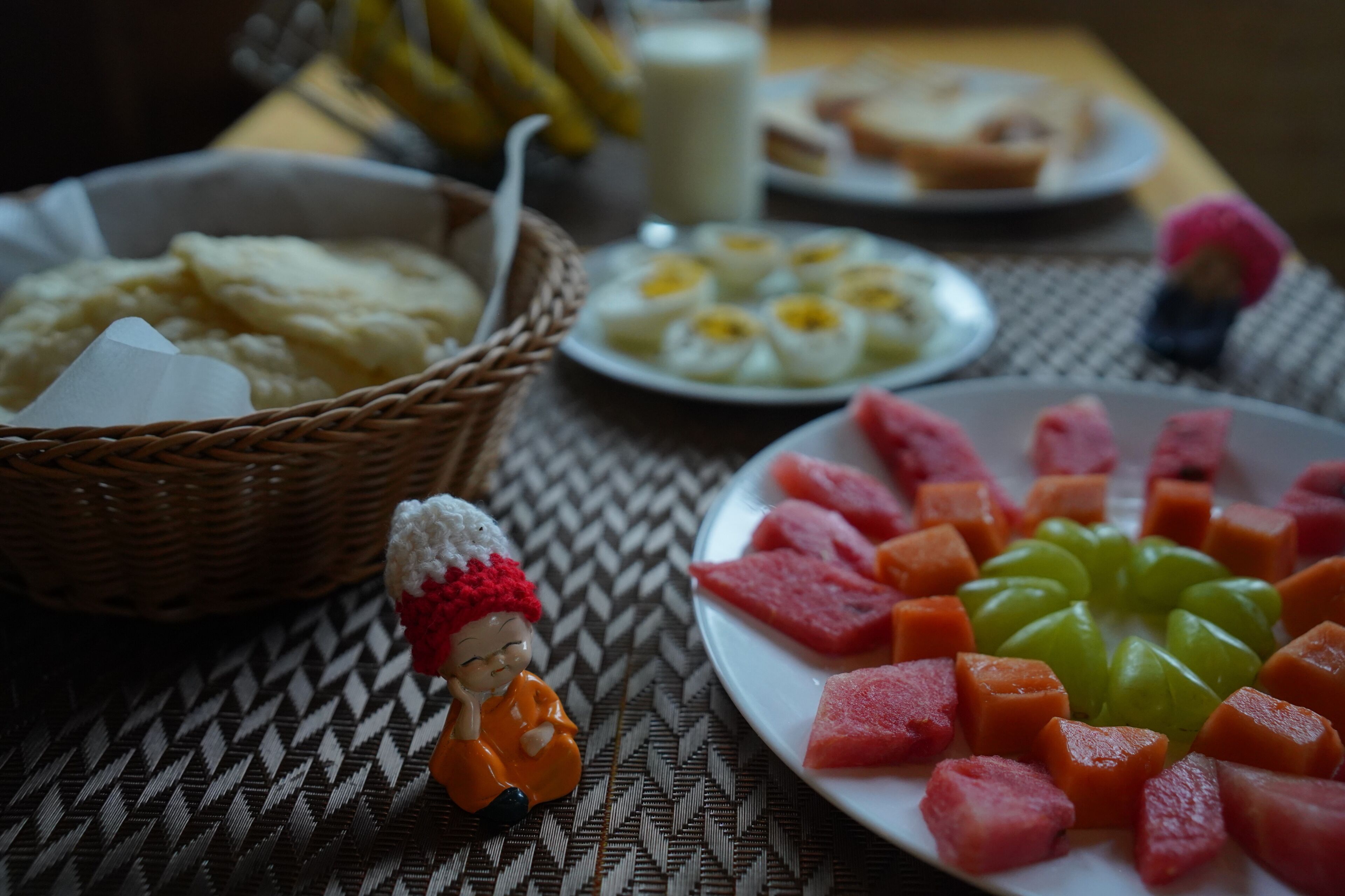 Una mesa con diferentes alimentos, incluyendo una porción de sandía, una cesta de puré de papas y un plato de huevos.