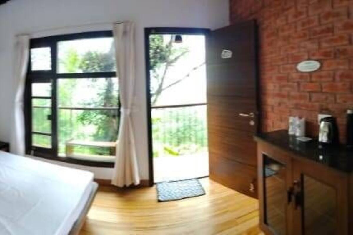 A bedroom with a bed, a wooden nightstand, a brick wall, and a window with curtains.