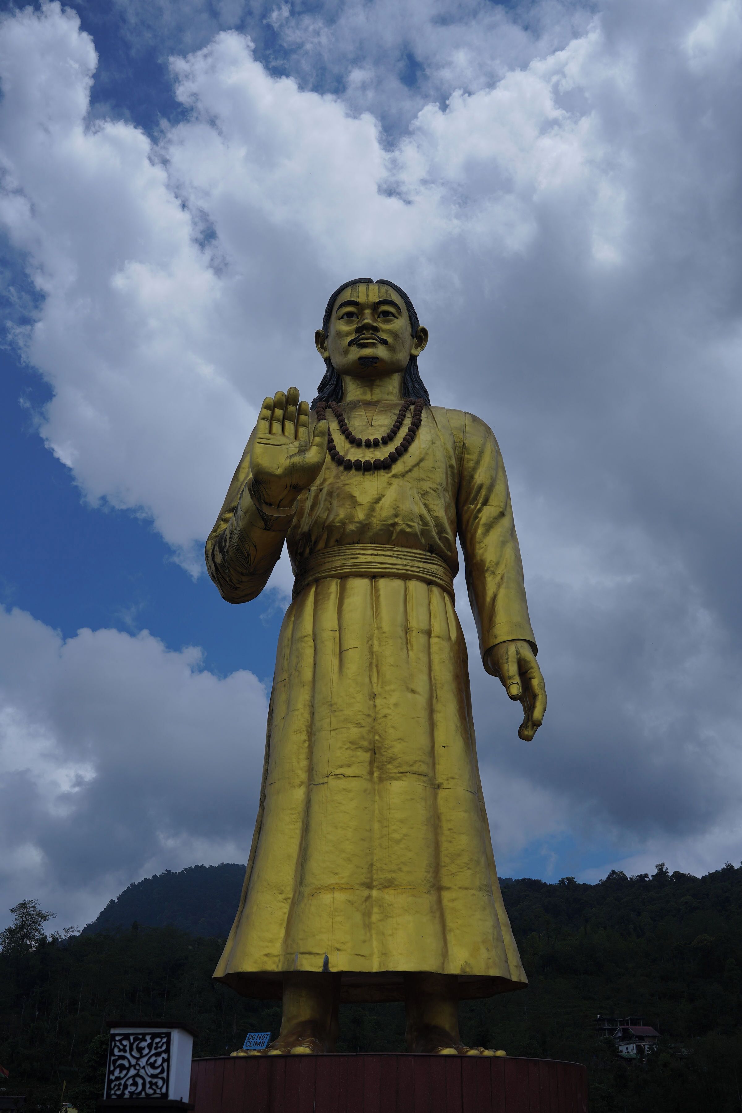 Une grande statue dorée, avec une main levée, se détachant sur un ciel nuageux.