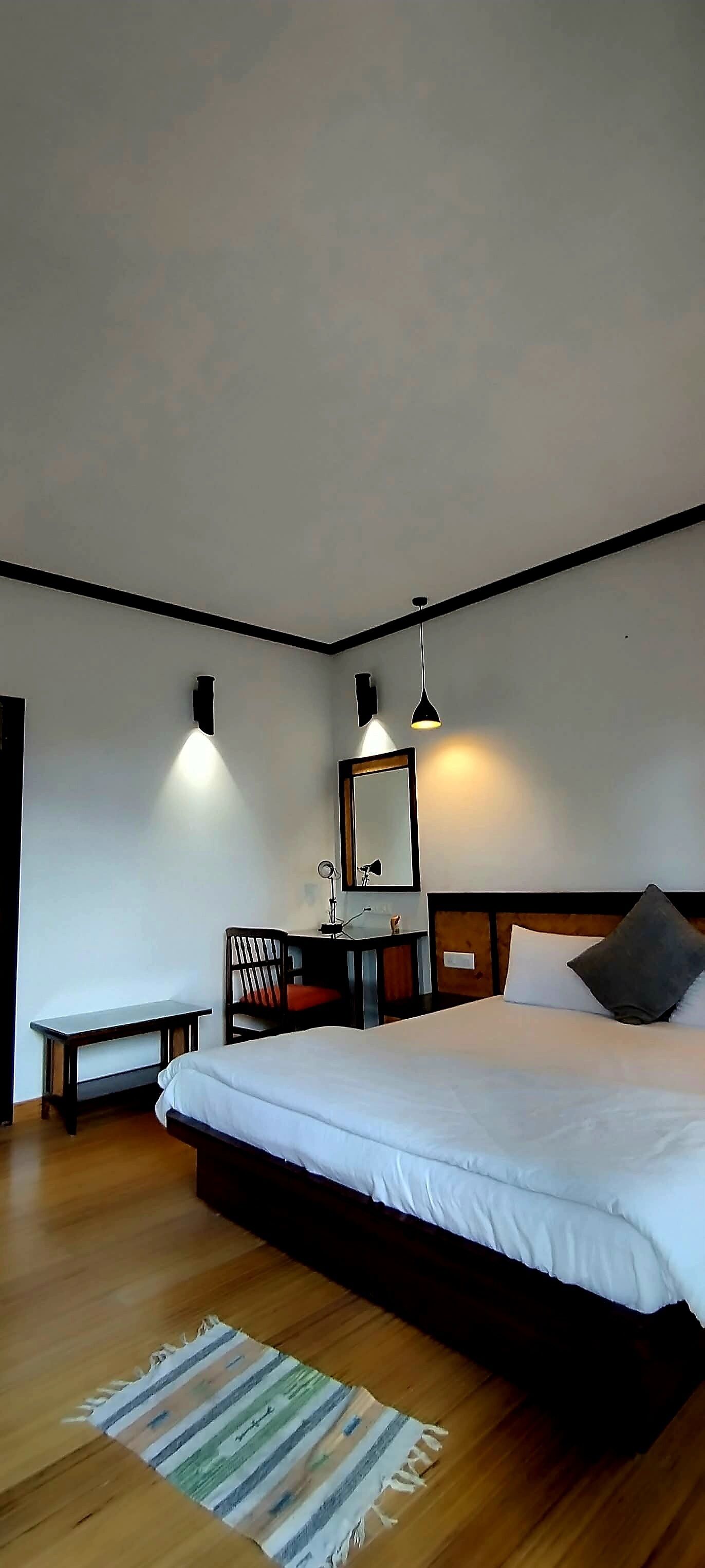 Quarto com uma cama grande, escrivaninha, cadeira, espelho e duas luminárias pendentes.