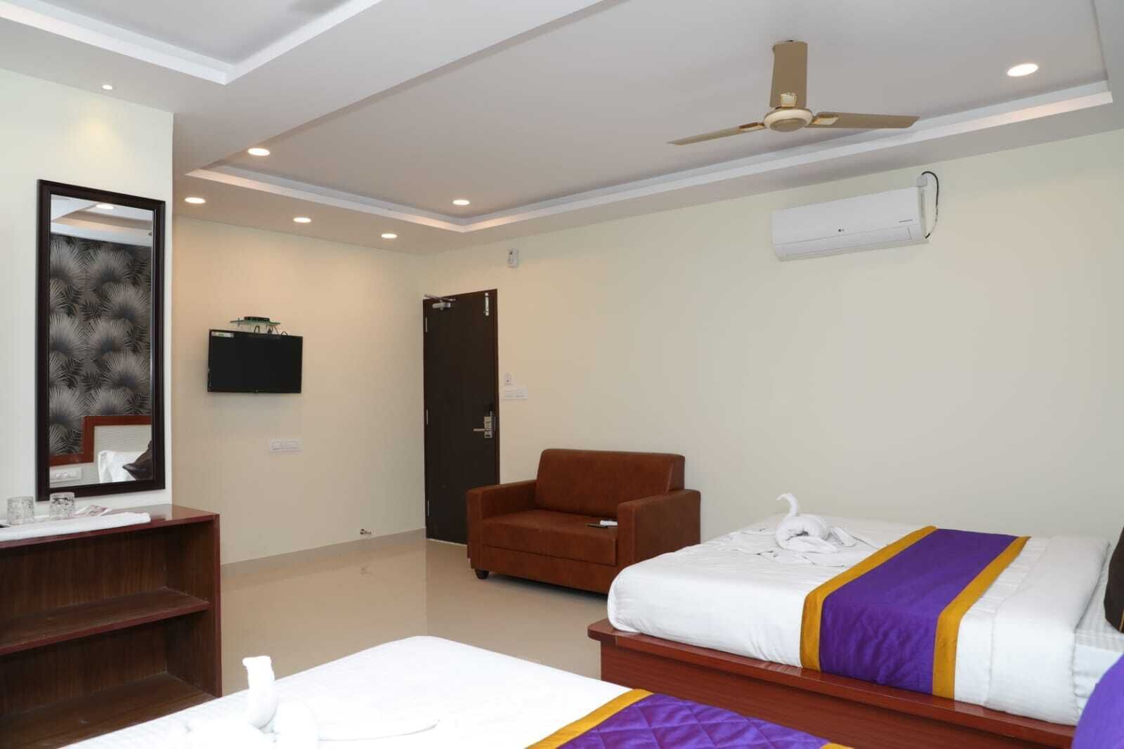 Una habitación de hotel con cama, una silla, un escritorio, un espejo y un ventilador de techo.
