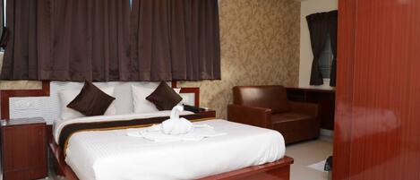 A hotel room with a large bed, a wooden headboard, a brown leather armchair, a wooden nightstand, and a wooden wardrobe.