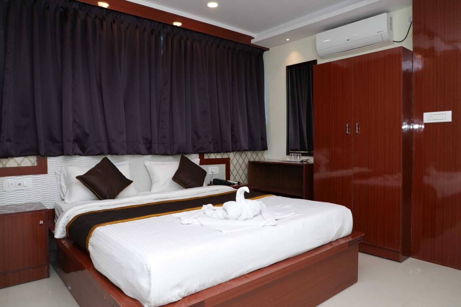Une chambre d’hôtel avec un grand lit, des rideaux occultants, une armoire en bois et un appareil de climatisation.