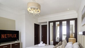 Une chambre d’hôtel avec un lit, une télévision, un lustre, une armoire et un miroir.