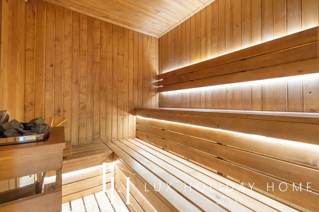 A wooden sauna with benches and a bench with a tray of rocks.