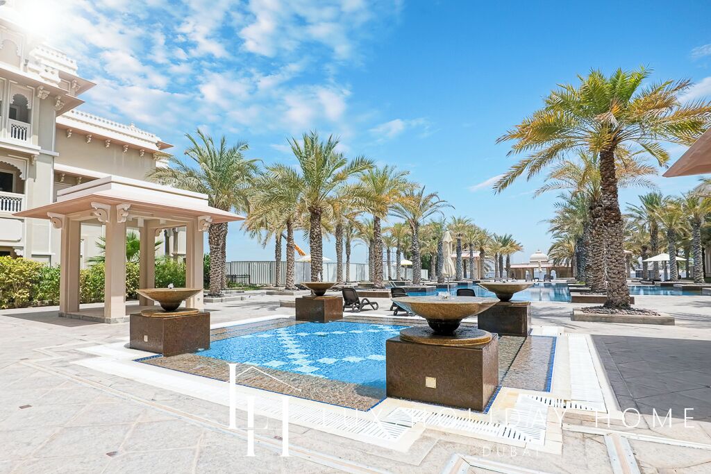 A resort pool area with palm trees, a gazebo, and a large fountain.