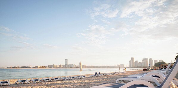 Una spiaggia con lettini, uno skyline cittadino sullo sfondo e un mare calmo.