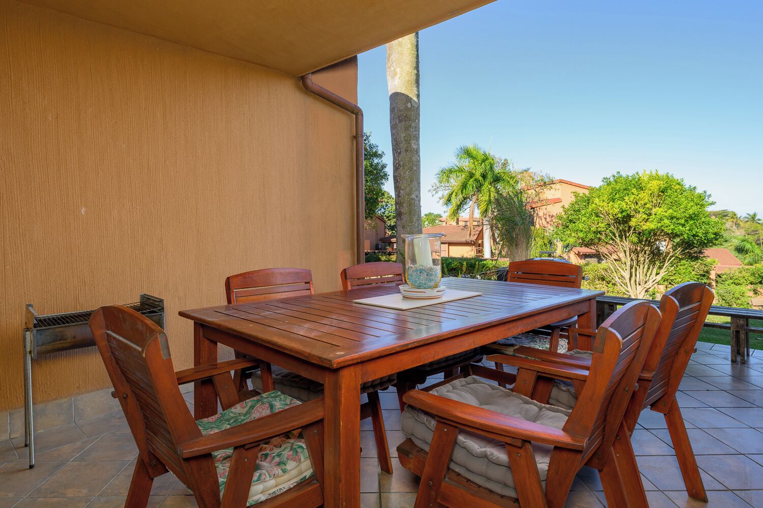 Une terrasse extérieure avec une table et des chaises en bois, un vase en verre rempli de fleurs et une vue sur le paysage environnant.