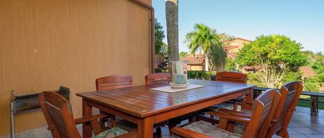 An outdoor patio with a wooden table and chairs, a glass vase with flowers, and a view of the surrounding landscape.