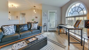 A modern living room with a black leather sofa, a coffee table, and a dining area with a table and chairs. There is a large arched window providing natural light. - Easy Access to Dtwn: High Point Condo (High Point)