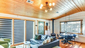 A cozy cabin interior with a wooden ceiling, a leather sofa, a dining table with chairs, and large windows offering a view of the outdoors. - Mtn-View Haven w/ Hot Tub: 9 Mi to Dtwn Bailey (Bailey)