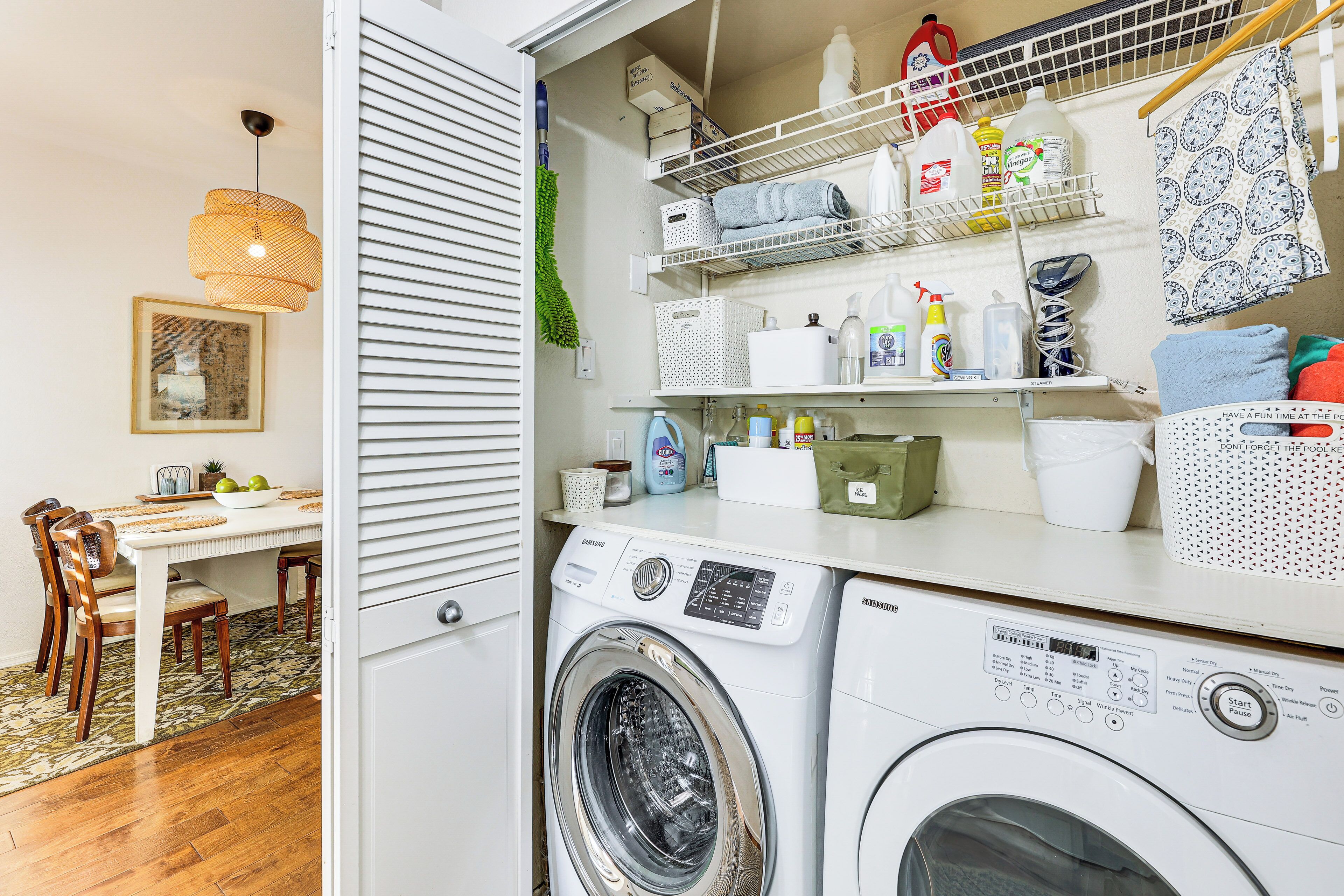 A laundry area with a washing machine, shelves with cleaning supplies, and a dining area with a table and chairs.