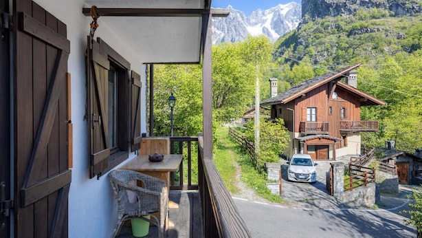 Un balcon donnant sur une montagne, une maison en bois et une voiture garée devant.