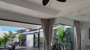 A spacious living area with a large glass door leading to an outdoor patio, a modern sofa, a glass coffee table, and a pool.