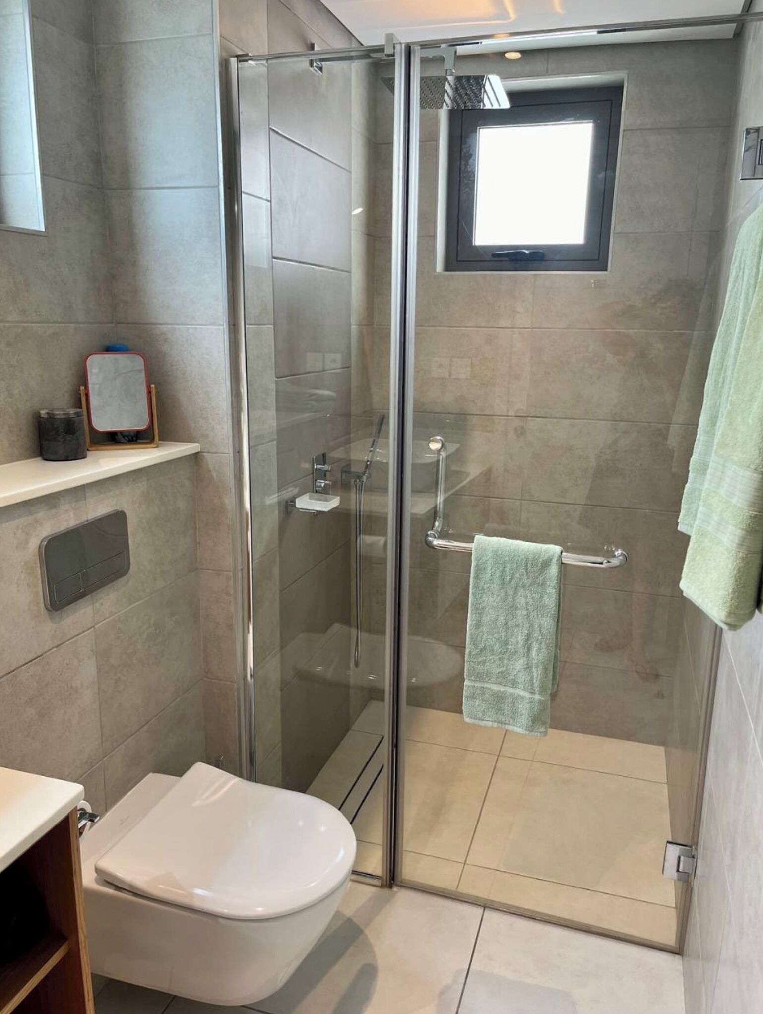 A modern bathroom with a glass-enclosed shower, a toilet, and a small window.
