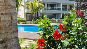Ein modernes Hotel mit Pool, Palmen und roten Blüten.