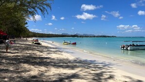 Ein Strand mit klarem türkisblauem Wasser, einem Sandufer und einigen Booten.