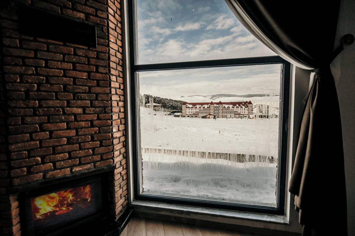 A room with a brick fireplace and a large window overlooking a snowy landscape.