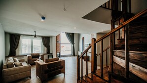 A spacious living area with a wooden staircase, a sofa set, and a large window with curtains. - Kayı Resort Hotel (Sarikamis)