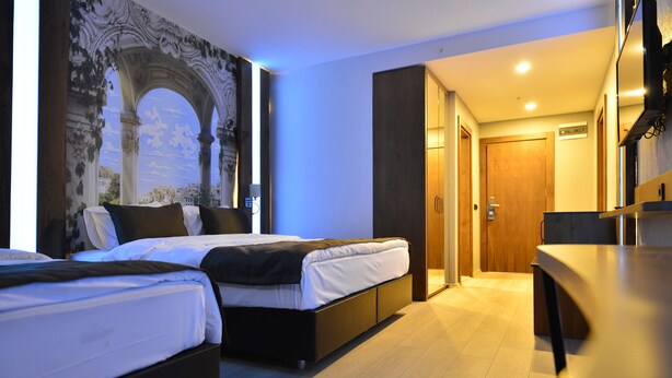 A modern hotel room with two beds, a dining area, and a large mural on the wall. - Kayı Resort Hotel (Sarikamis)