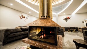 A modern lounge with a central fire feature, plush seating, and a unique ceiling design. - Kayı Resort Hotel (Sarikamis)