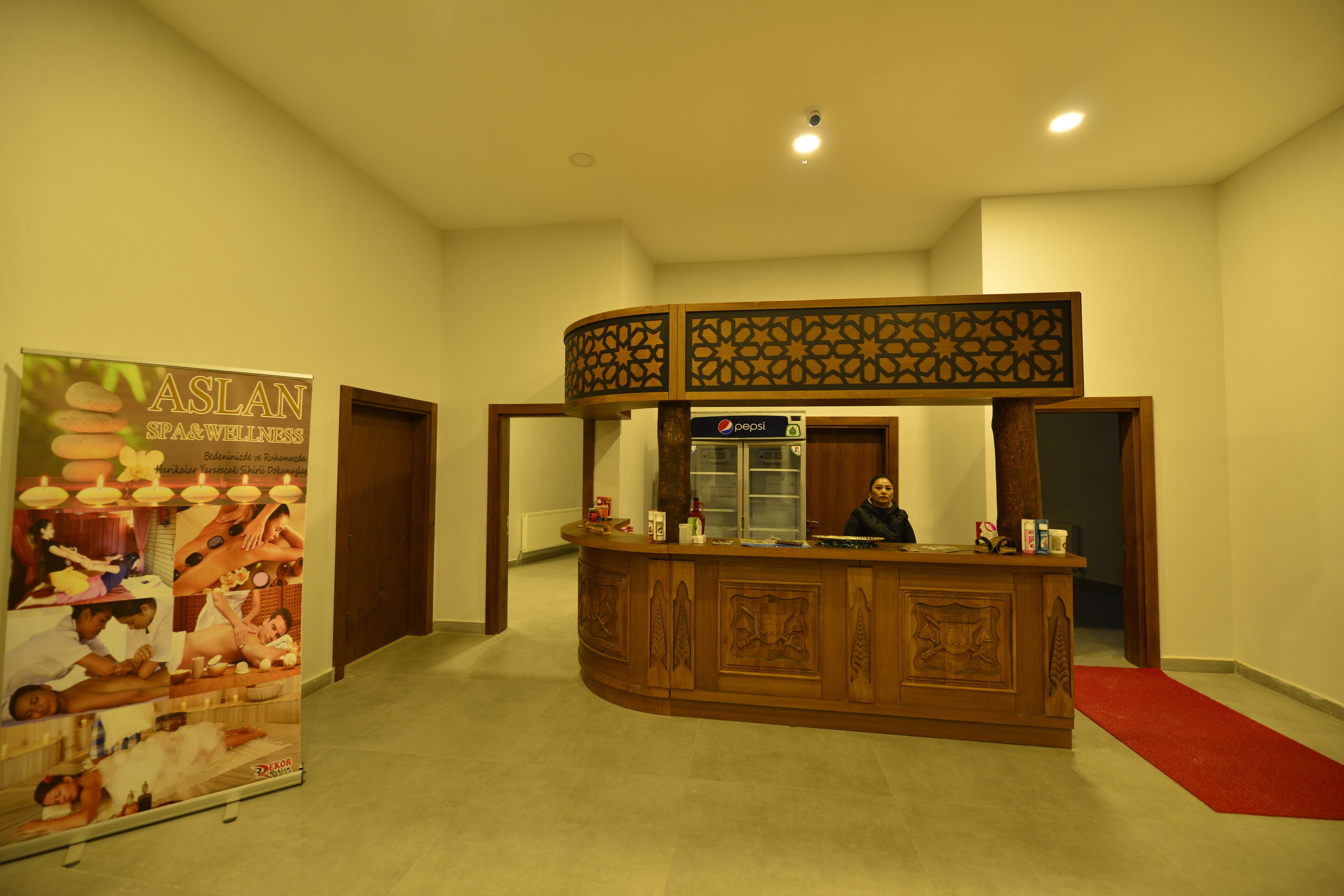 A reception area with a wooden counter, a Pepsi refrigerator, and a poster advertising ASLAN SPA & WELLNESS.