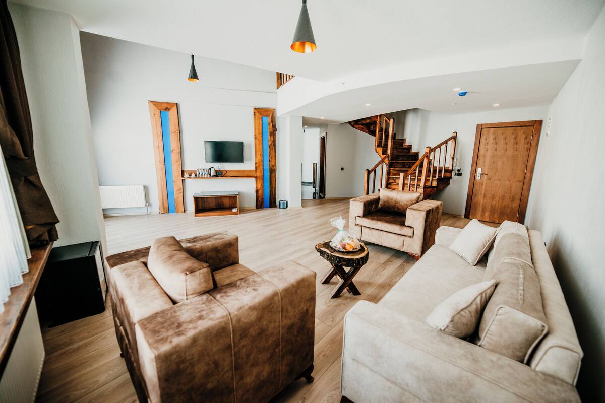 A spacious living area with a wooden staircase, a sofa set, and a television.