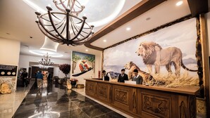 A lobby with a reception desk, a chandelier, a large lion mural, and a polished floor. - Kayı Resort Hotel (Sarikamis)