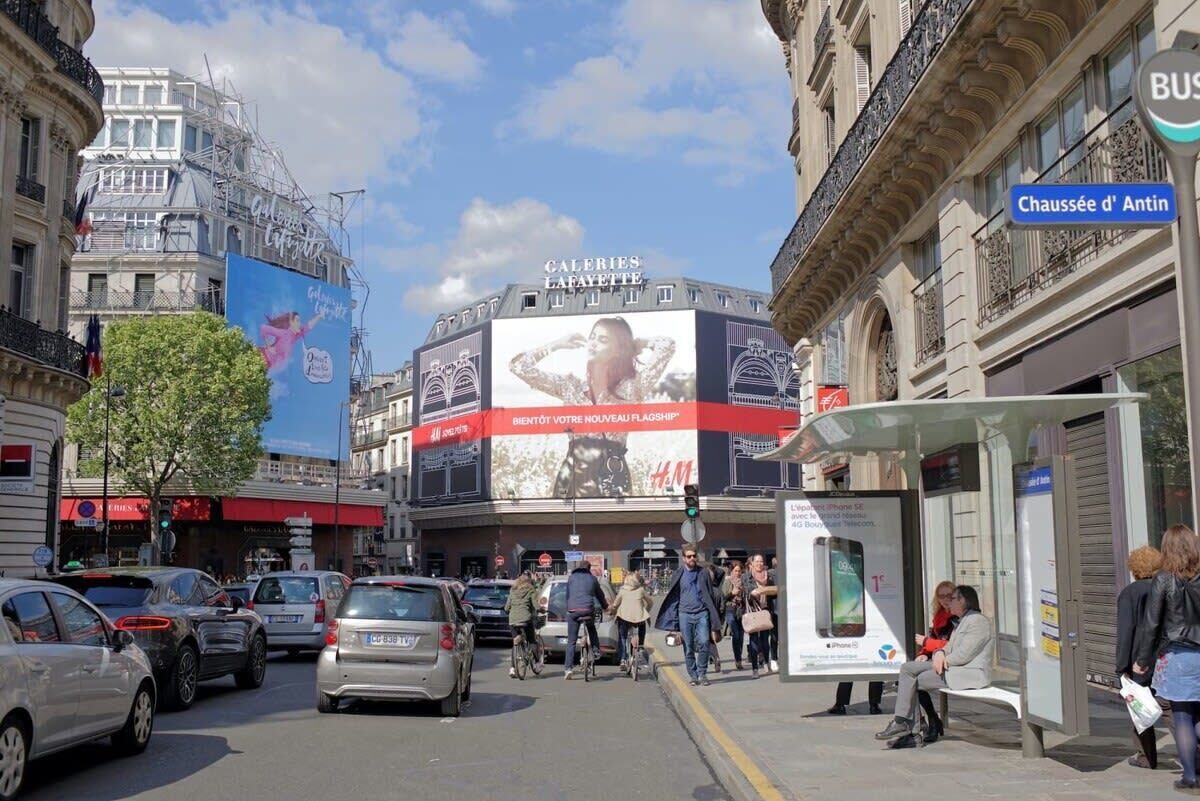 A busy urban street with a large billboard advertising a new fashion brand.