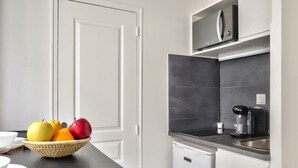 A kitchen with a black countertop, a coffee maker, and a microwave on the shelf. - Cosy Mezzanine Studio in the Heart of Paris (4) (Paris)