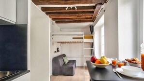 A modern kitchen with a built-in oven, a dining area with a table set for breakfast, and a cozy seating area with a sofa. - Cosy Mezzanine Studio in the Heart of Paris (4) (Paris)