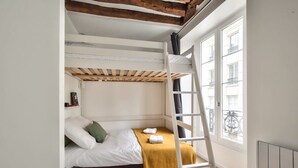 A bunk bed room with a wooden ladder, white walls, and a window overlooking a balcony. - Cosy Mezzanine Studio in the Heart of Paris (4) (Paris)