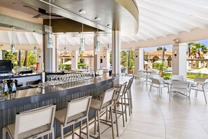 Eine moderne Außenbar mit gebogener Theke, Barhocker und hängenden Pendelleuchten.