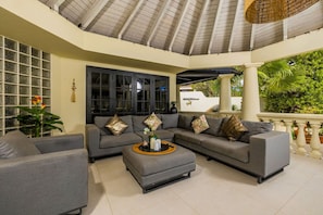 A spacious living area with a grey sectional sofa, a matching ottoman, and a large window with a view of greenery.